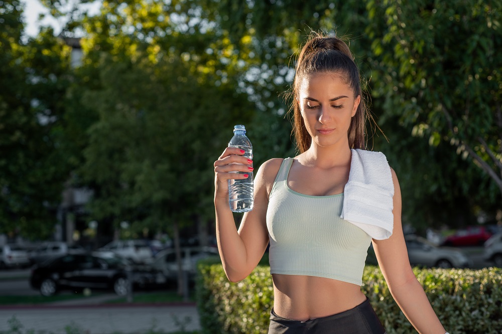 Woman in running clothes outside holding up a water bottle